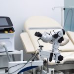 Close-up of colposcope, over background gynecological consultation room with gynecology chair. Colposcopy, examination of cervix